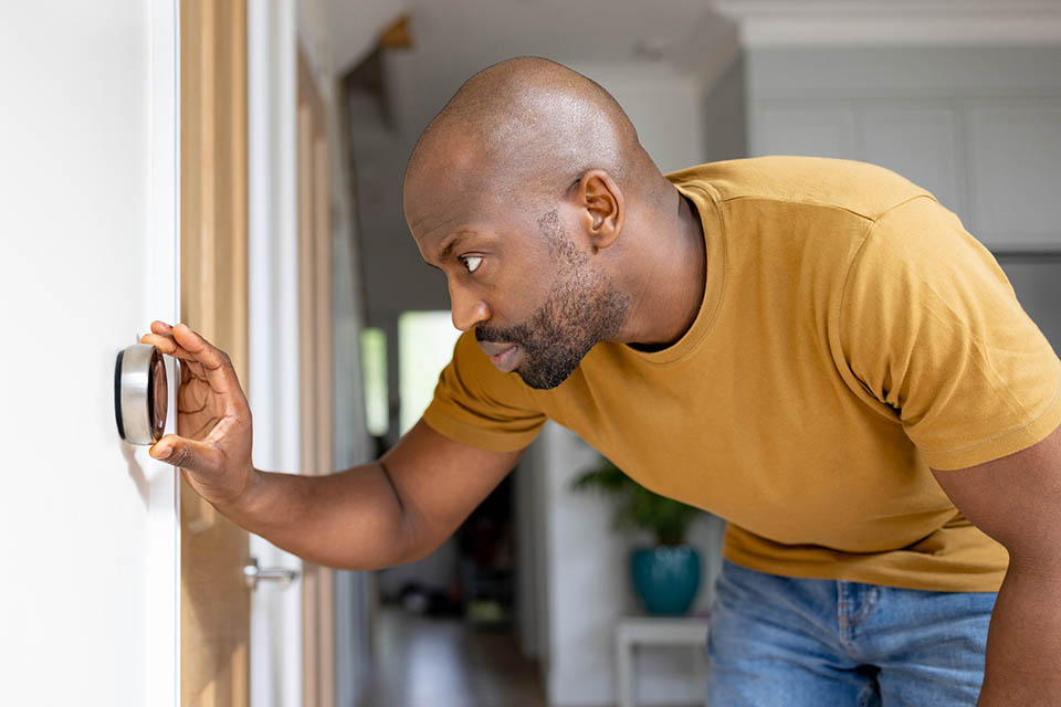 African American man adjusting the temperature on the thermostat of his house - home automation concepts