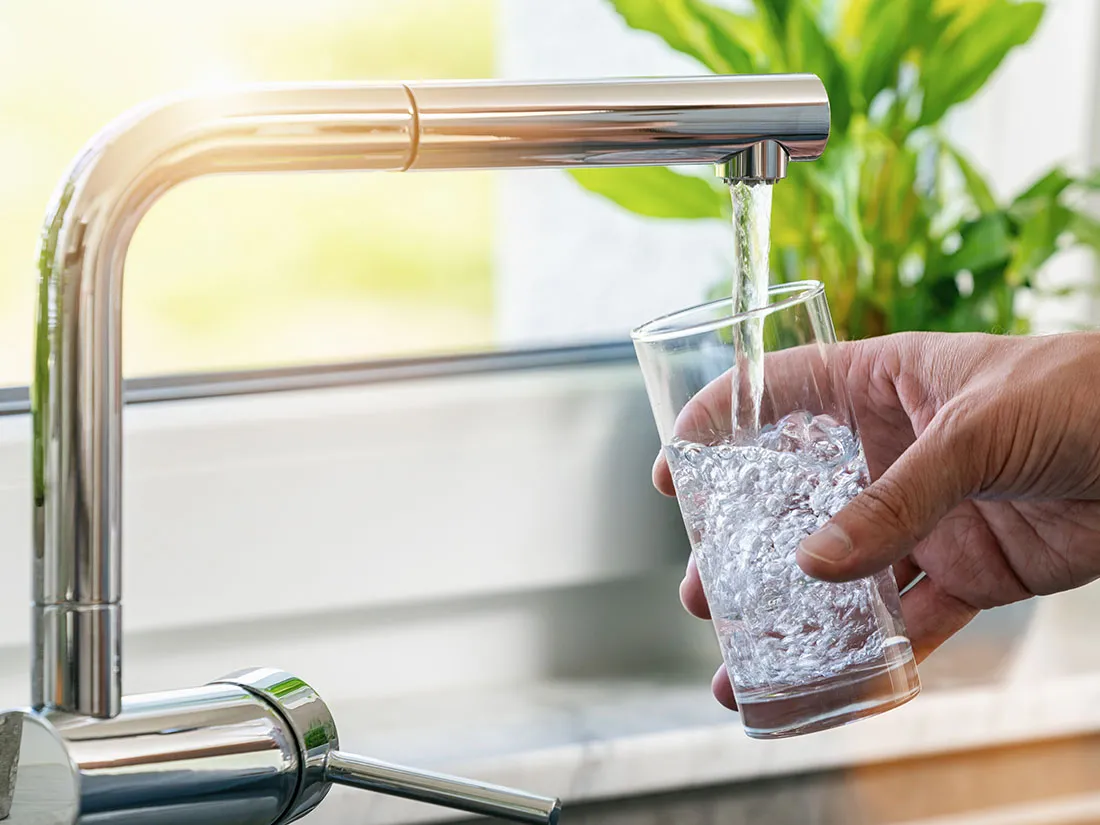 Hand holding a glass of water poured from the kitchen faucet