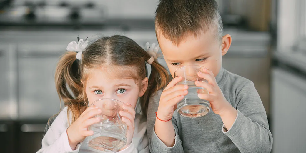 Two children drinking from glasses of water