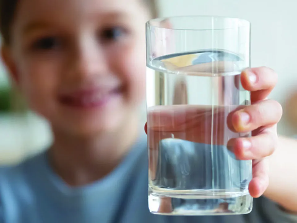 Close up of happy little girl holding a glass of water